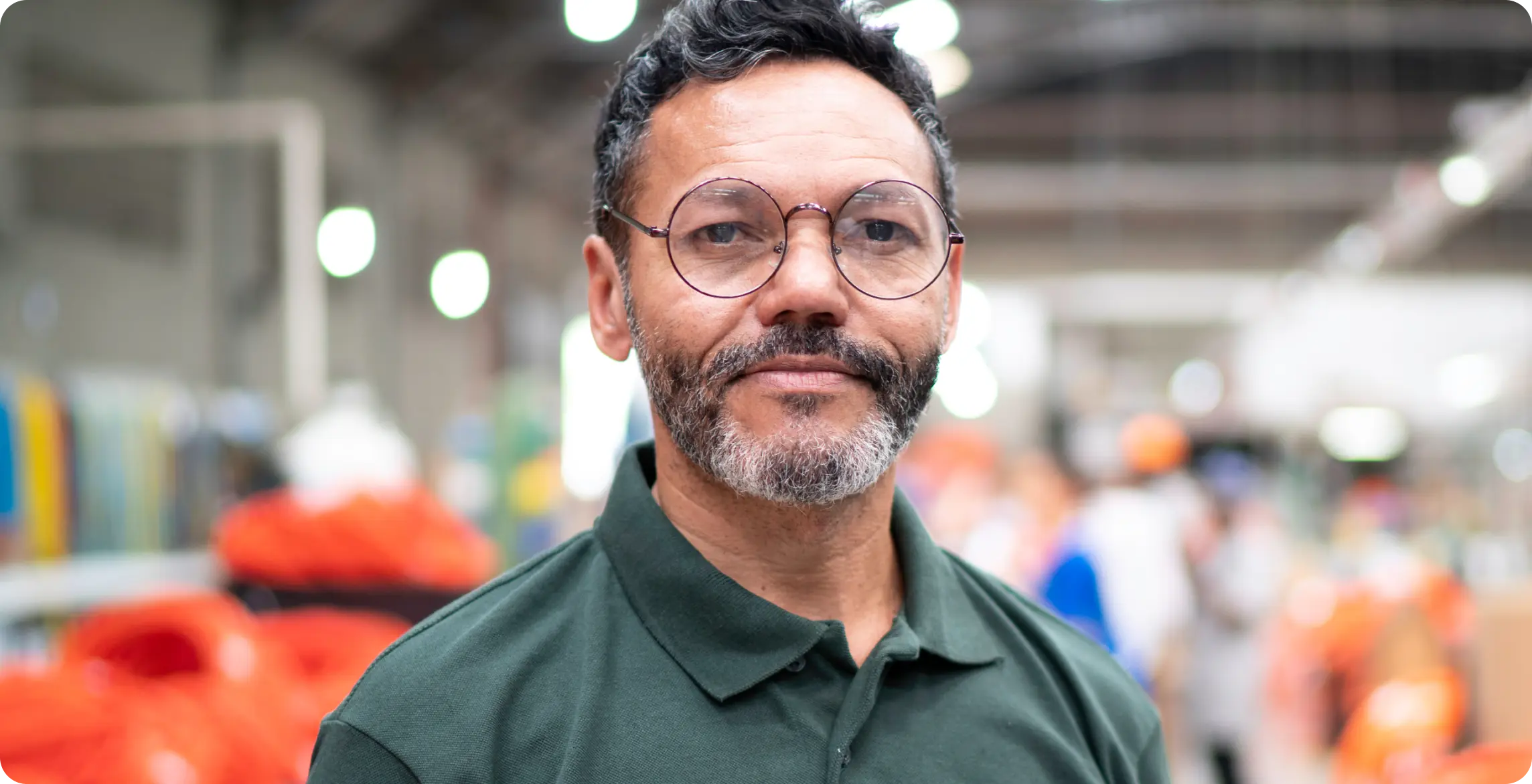 A man in a green polo shirt and glasses standing in a factory.