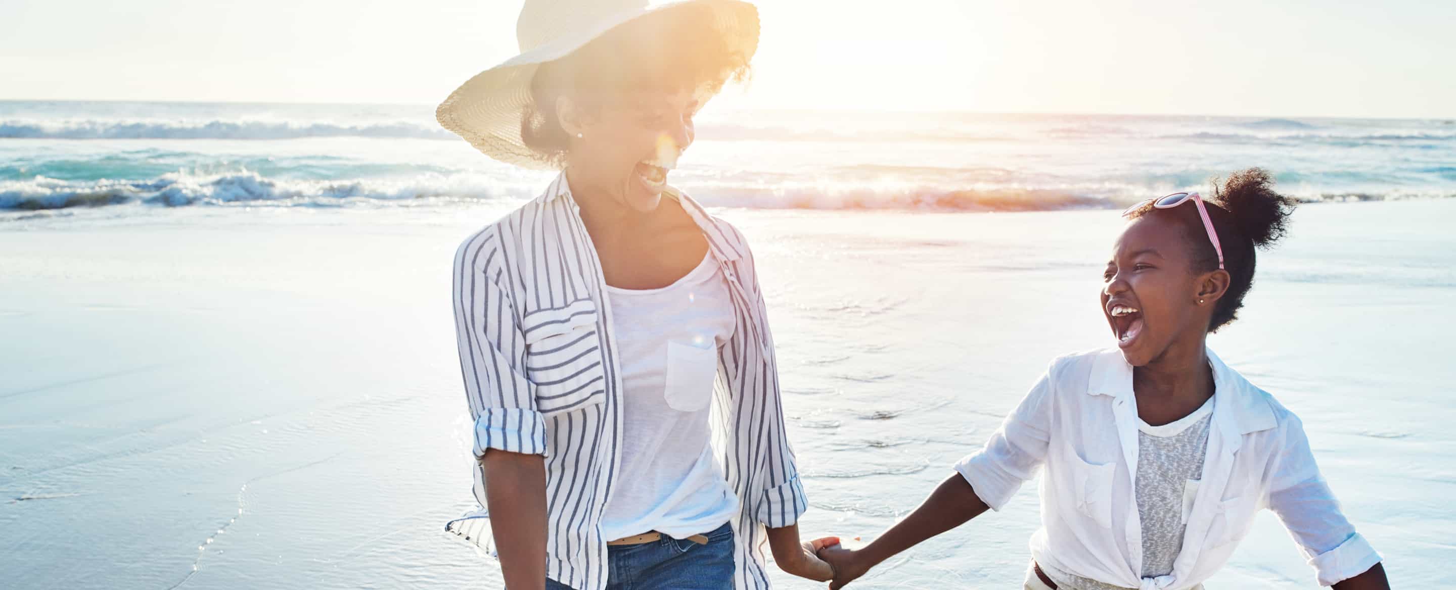 Mother and daughter holding hands and laughing on the beach during sunset